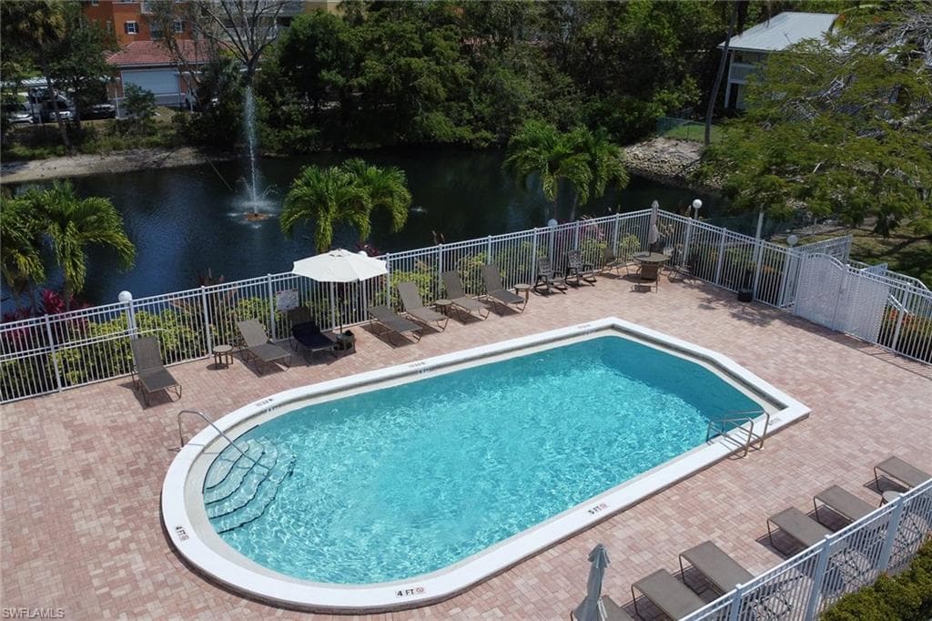 Community pool with a patio area, fence, and a water view