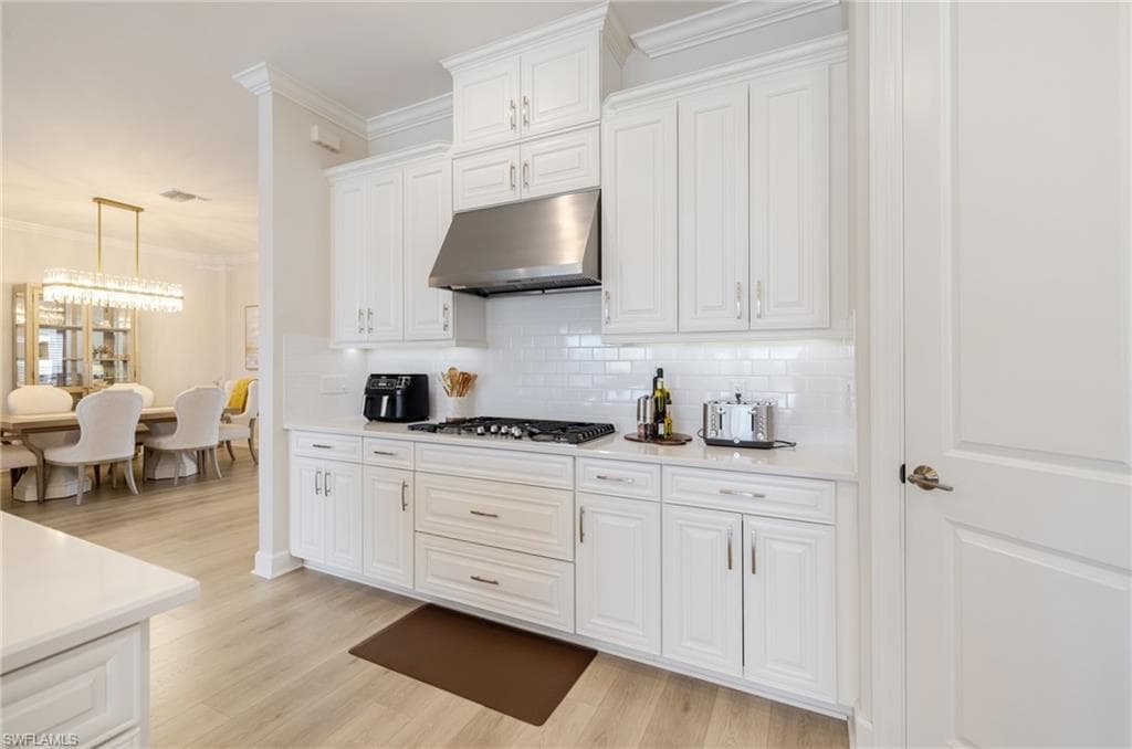 Kitchen with ornamental molding, white cabinets, light wood-type flooring, backsplash, and stainless steel gas stovetop