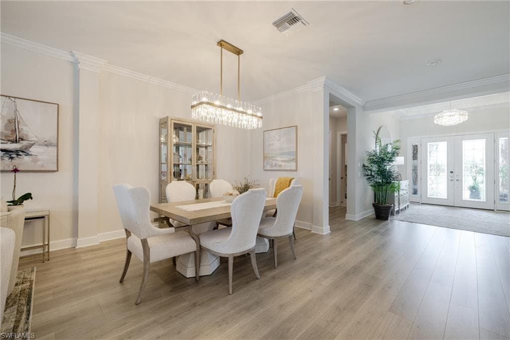 Dining area featuring hanging lights, french doors, ornamental molding, and light wood-type flooring