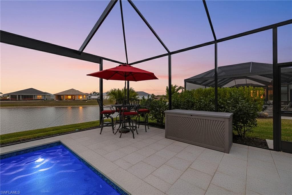 Swimming pool with glass enclosure, outdoor dining area, a sunroom, and a water view