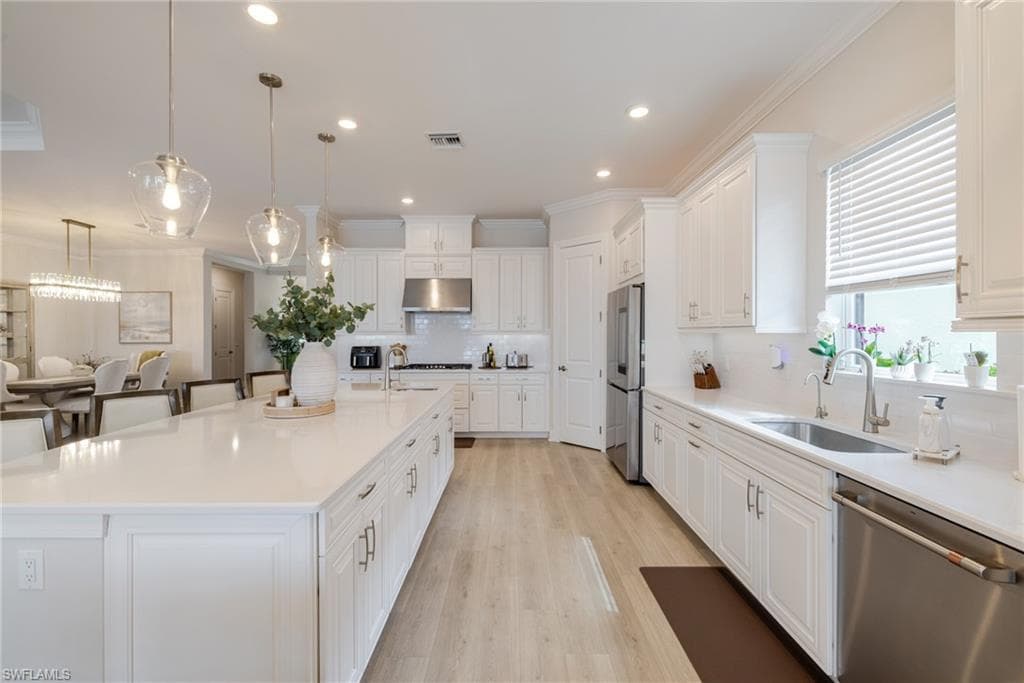 Kitchen with white cabinetry, stainless steel appliances, a large island with sink, and crown molding