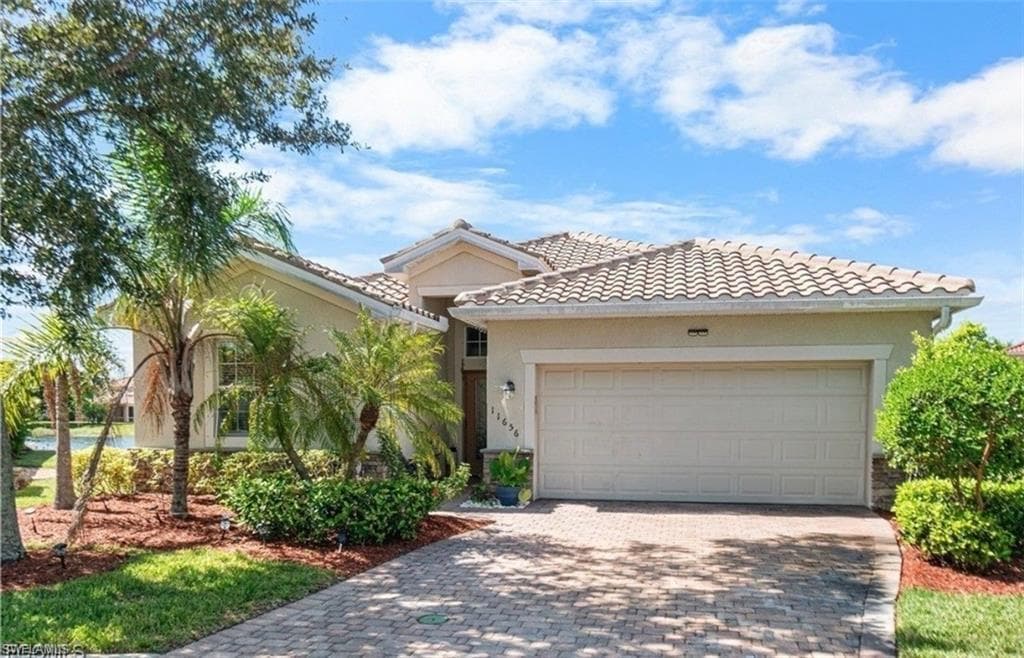 View of front of home featuring an attached garage, driveway, a tile roof, and stucco siding