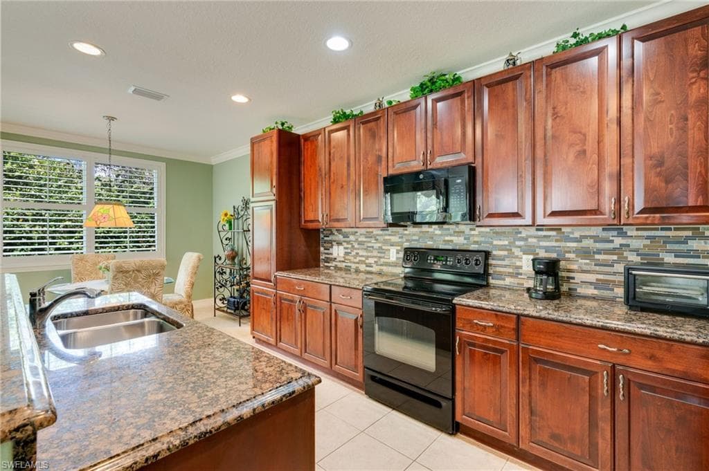 Kitchen featuring black appliances, dark stone counters, hanging light fixtures, crown molding, and light tile patterned floors