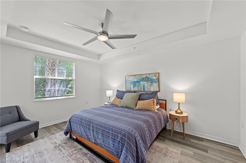 Bedroom featuring tray ceilings, a ceiling fan, and a window with blinds