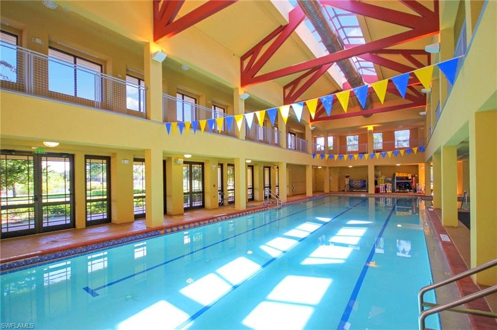 Indoor swimming pool featuring a skylight, high ceilings with exposed beams, and glass doors providing views of the outdoors