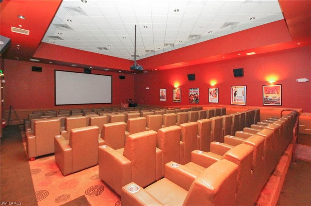 Entertainment room featuring a large projection screen, rows of upholstered seating with cup holders, and decorative wall sconces