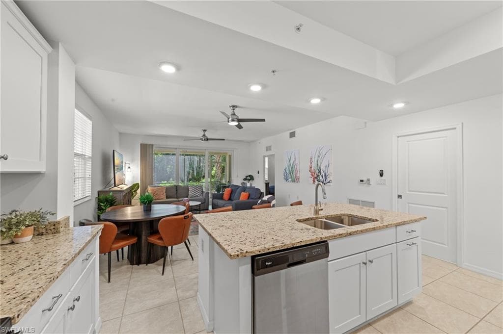 The property features a kitchen with granite countertops, white cabinetry, and a stainless steel dishwasher, opening to a living area with tile flooring and a view of exterior landscaping
