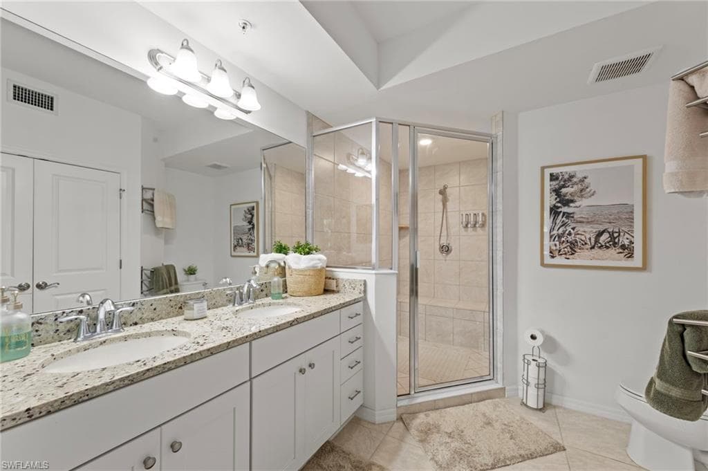 The bathroom features a double vanity with granite countertops, a large mirror, and a glass-enclosed shower with tiled walls