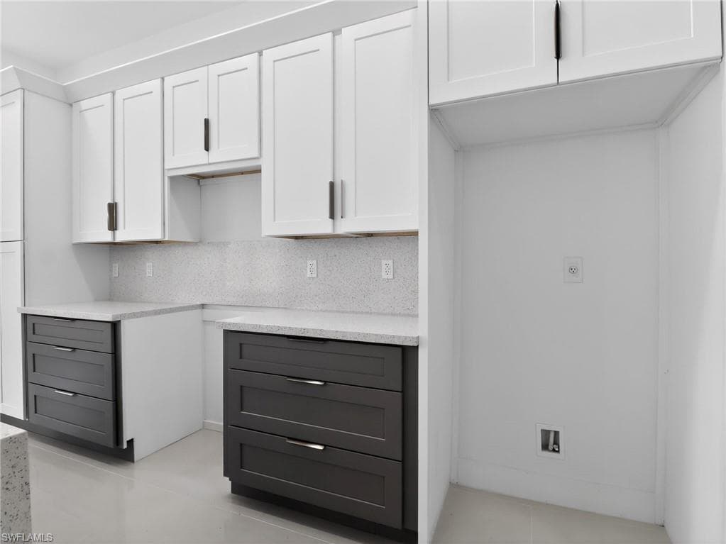 Kitchen featuring white upper cabinetry, dark lower cabinetry, light-colored countertops, and a matching backsplash