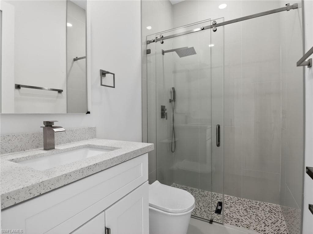 This bathroom features a contemporary vanity with a speckled countertop, a modern faucet, and a spacious shower with a glass enclosure and rain shower head