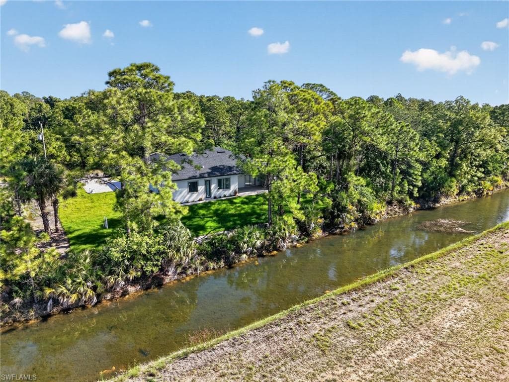 Waterfront property featuring a single-story residence with a dark shingle roof, white siding, and dark-framed windows