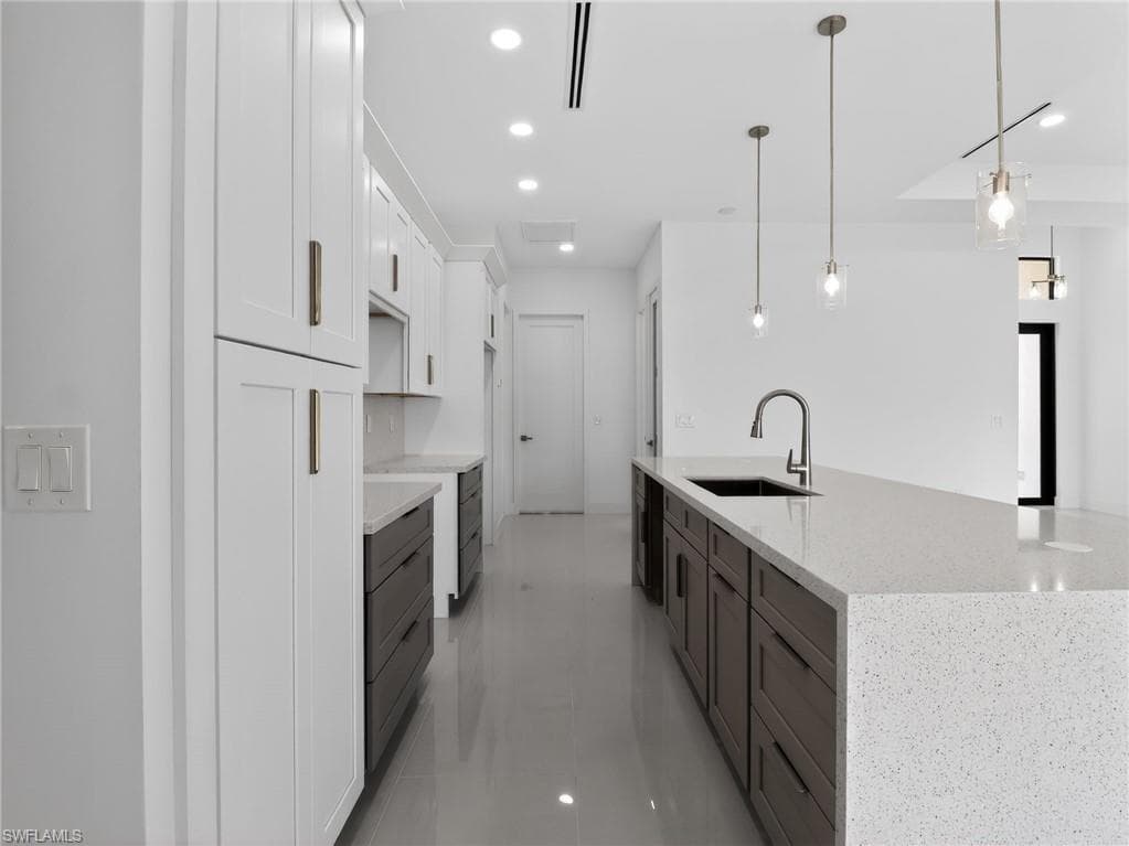 The kitchen features white shaker style upper cabinetry, dark lower cabinetry, light-colored countertops, a kitchen island with an integrated sink, and pendant lighting