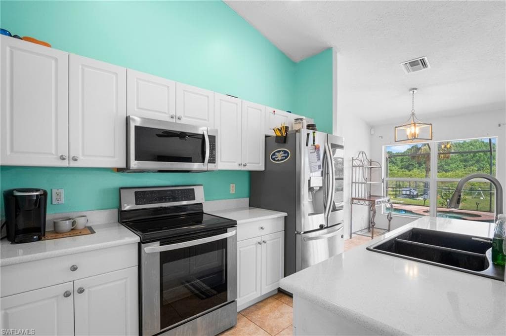 Kitchen with stainless steel appliances, a sink, white cabinetry, hanging light fixtures, and light countertops