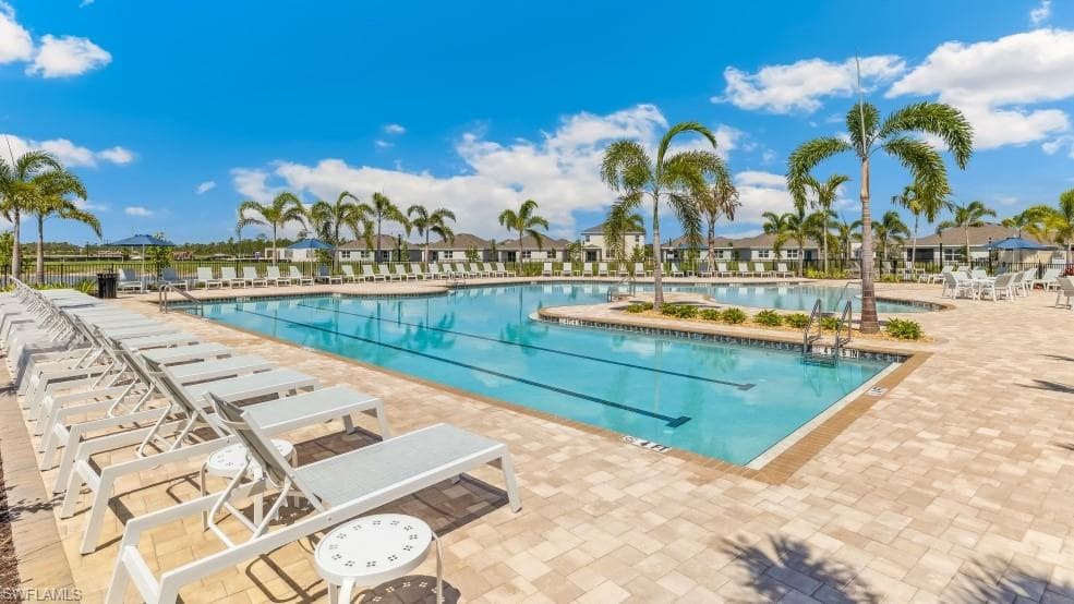 Expansive outdoor swimming pool with a paved deck, surrounded by numerous lounge chairs and palm trees