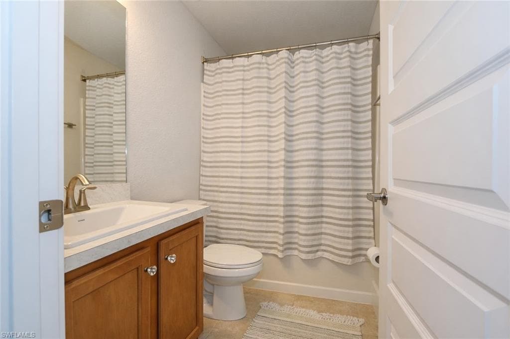 Bathroom featuring a vanity with a white countertop and wood cabinetry, a toilet, and a shower with a striped curtain