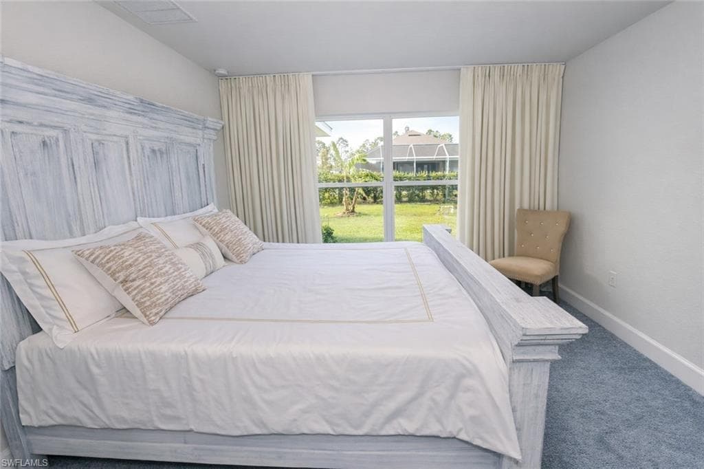 Bedroom featuring carpeted flooring and large windows with privacy curtains, overlooking a landscaped yard