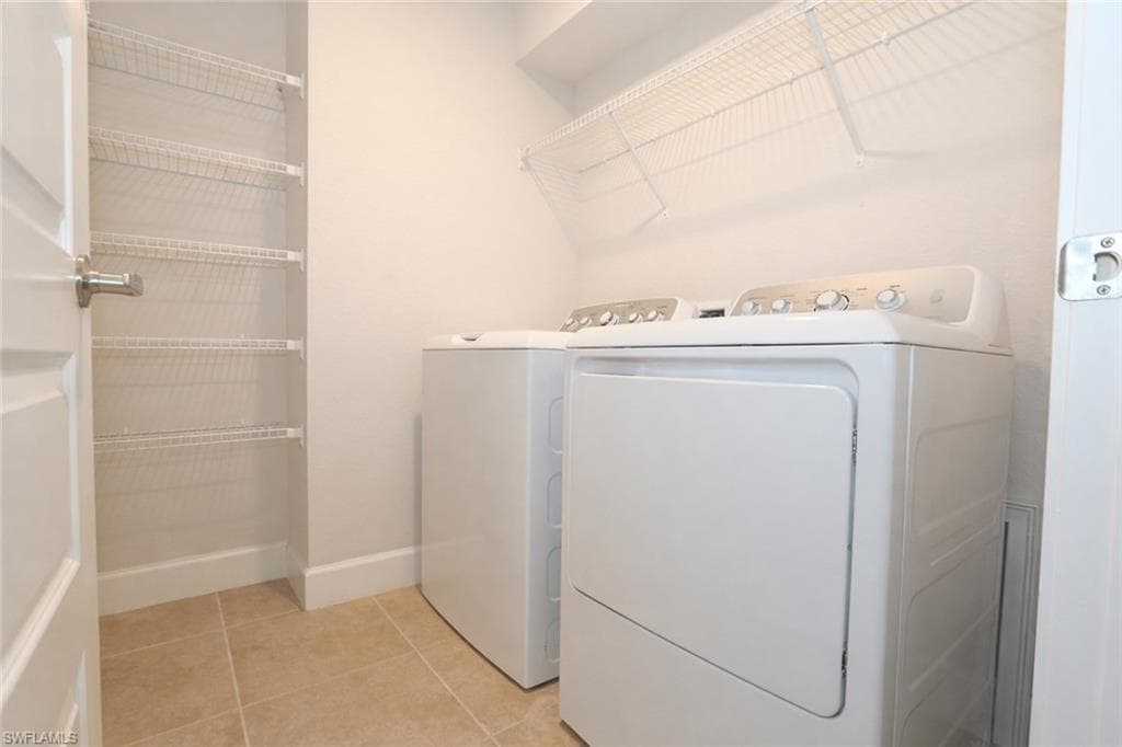 This utility area features white walls, tiled flooring, a washer and dryer, and wire shelving for storage