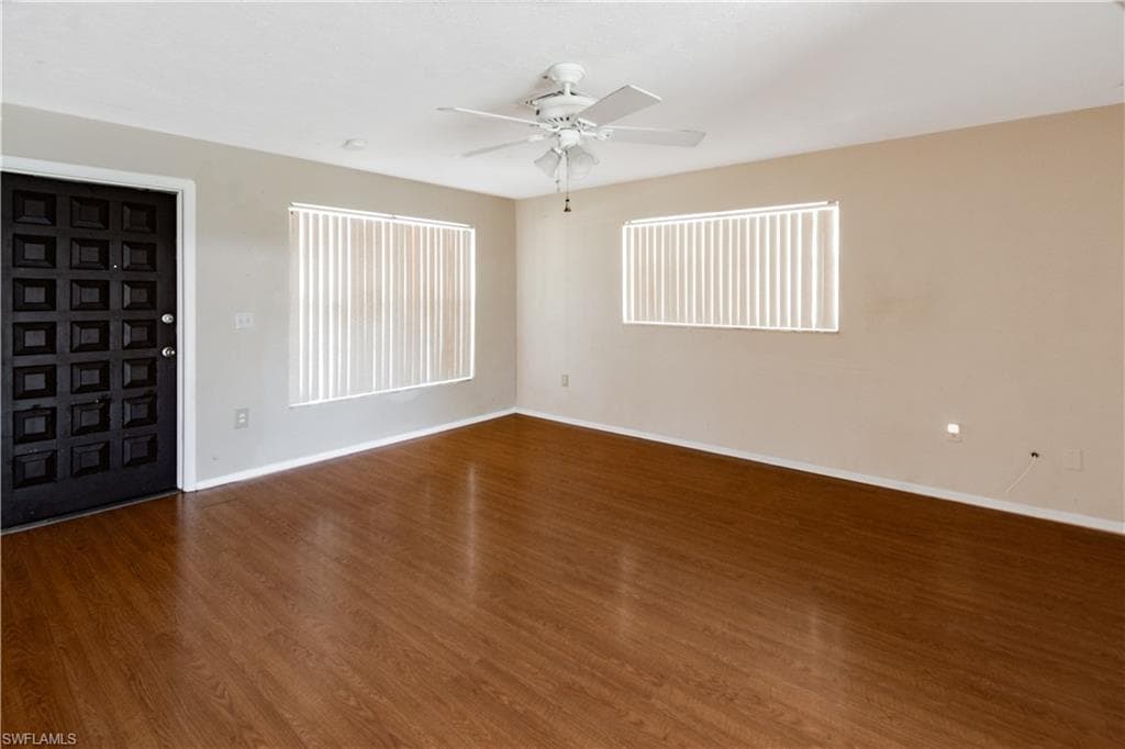 Spacious living room featuring vinyl flooring, a ceiling fan, and two windows with vertical blinds