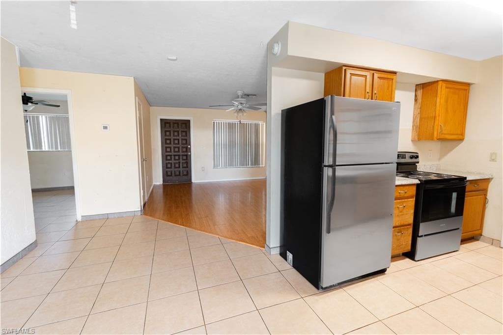The kitchen features tile flooring, wood cabinetry, a stainless steel refrigerator, and a range