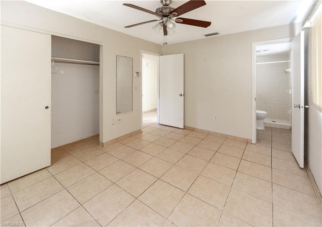 The primary bedroom features light-colored tile flooring, a ceiling fan, and a spacious closet with sliding doors