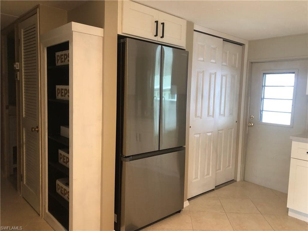 Kitchen featuring white cabinetry with quiet close, stainless steel refrigerator, and light tile patterned flooring