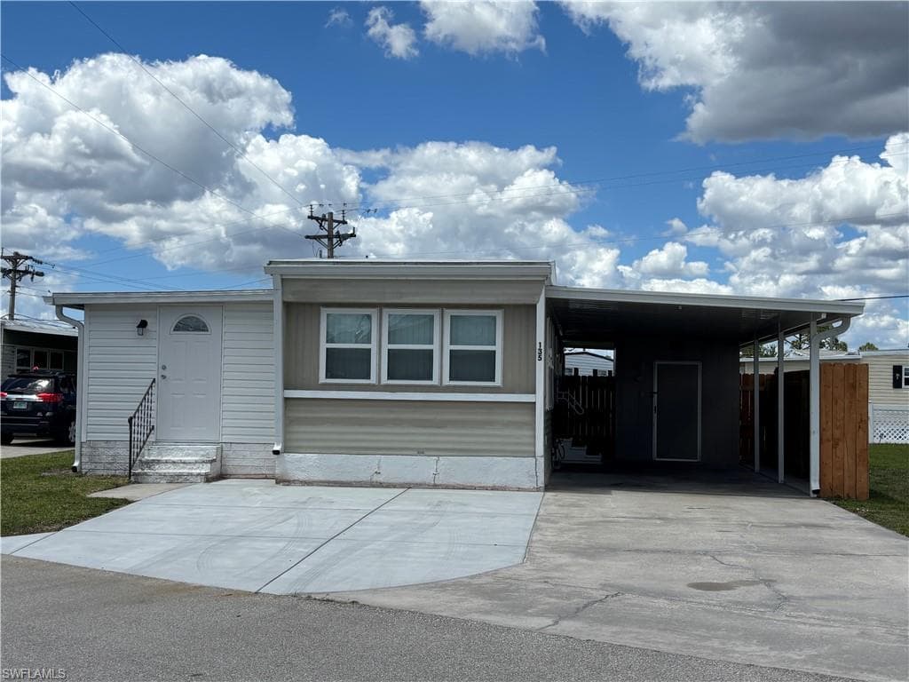The property features a light-colored exterior with a front entry door and a covered carport area