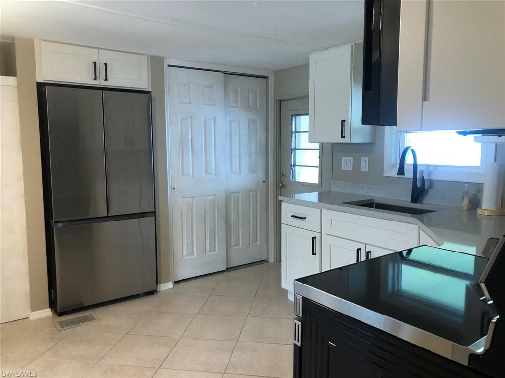 Kitchen featuring stainless steel appliances refrigerator, sink, and white cabinets