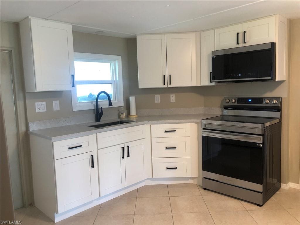 Kitchen featuring sink, light tile patterned floor, quartz countertops, appliances with stainless steel finishes, and white cabinets