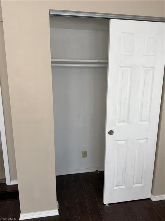 Closet featuring a white sliding panel door, interior shelving, and a hanging rod, all set against a neutral wall color and dark wood-finish flooring