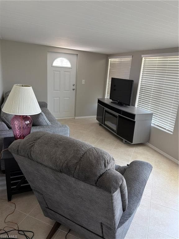 Living area featuring a white entry door with an arched glass insert, two windows with horizontal blinds, light tile flooring, and light gray wall paint