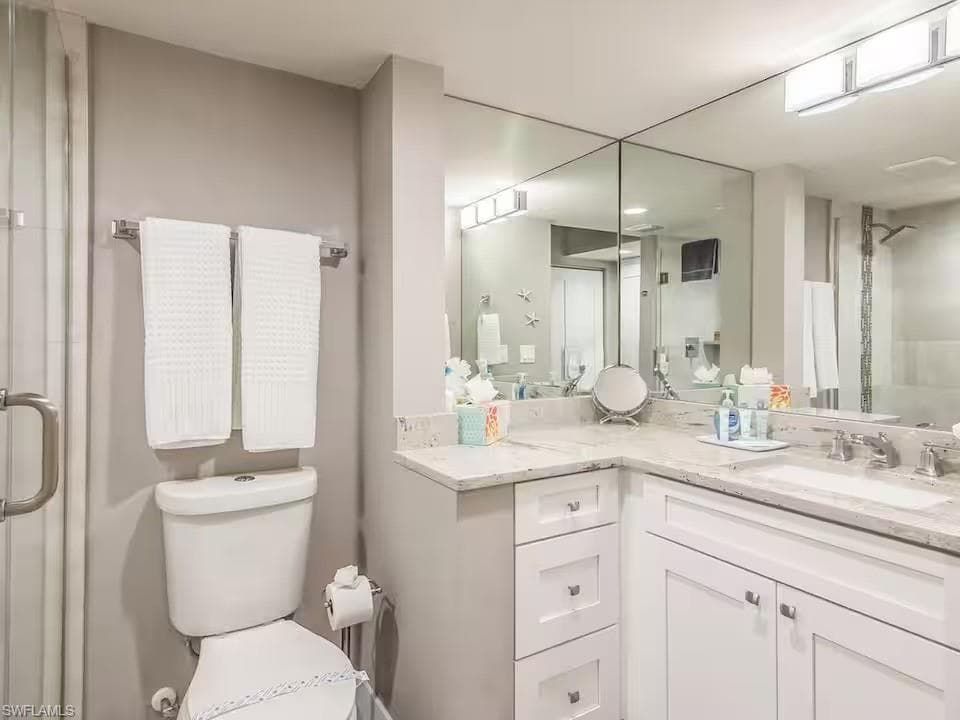 Bathroom featuring a light-colored vanity with a sink, reflective mirrored walls, and a toilet