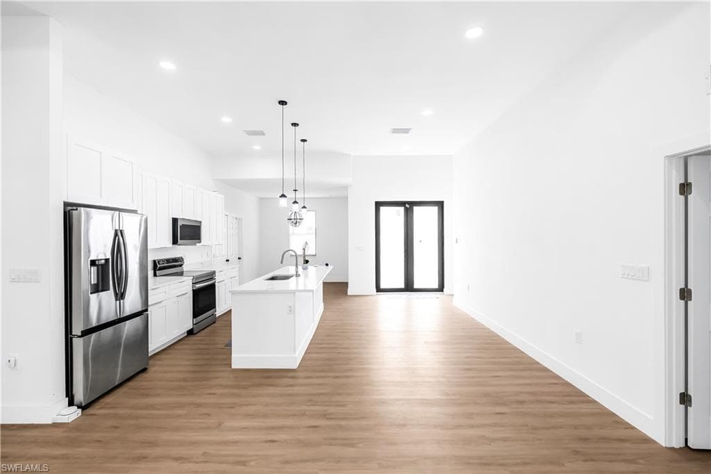 Open-concept living area featuring wood-finish flooring, recessed lighting, and a white kitchen island with pendant lighting
