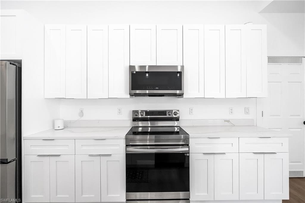Modern kitchen featuring white shaker cabinetry, stainless steel appliances, light-toned countertops, and a full suite of upper and lower storage