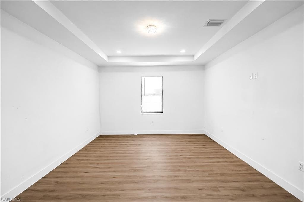 Spacious room featuring wood-finish flooring, crisp white walls, and a recessed ceiling with integrated lighting