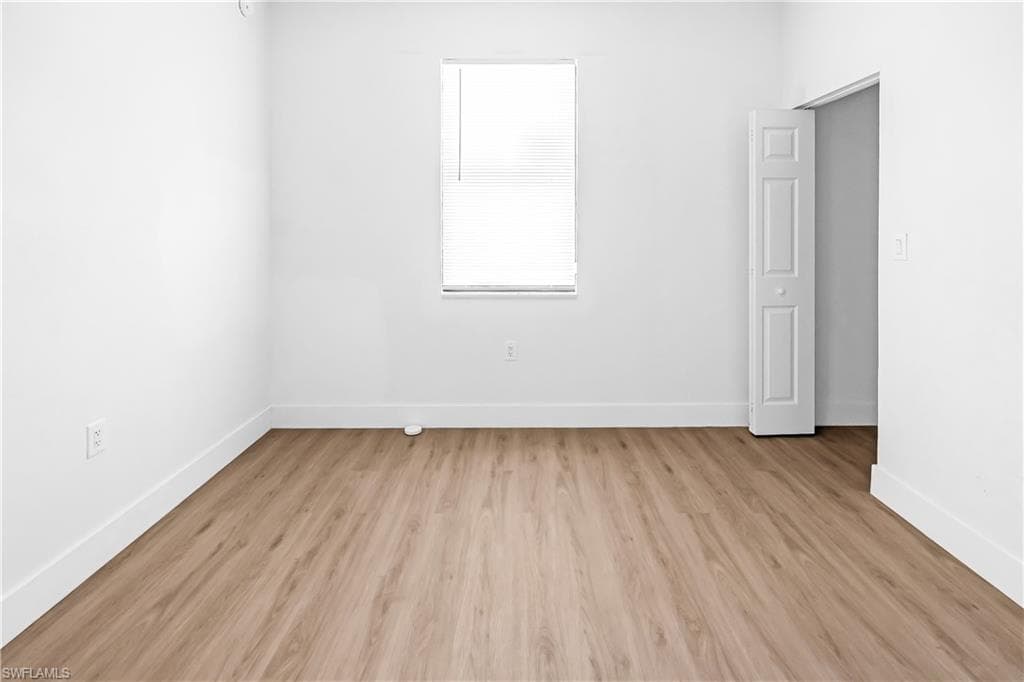 Room featuring light wood-finish flooring, white painted walls, and a window with horizontal blinds