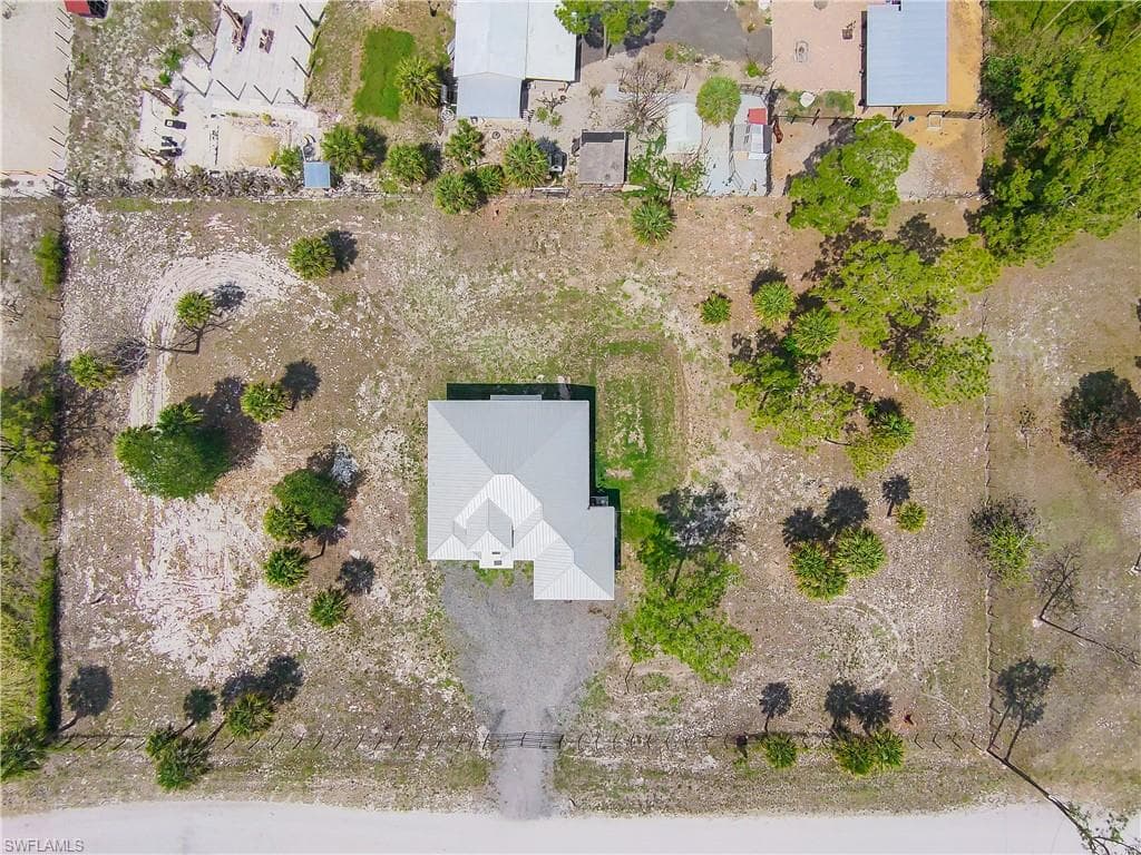 Aerial perspective showcasing a single-story residence with a light gray metal roof situated on a gravel drive