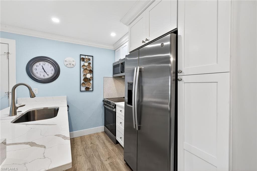 Kitchen featuring white shaker-style cabinetry, stainless steel appliances, light-toned countertops with veining, a stainless steel undermount sink, and wood-finish flooring