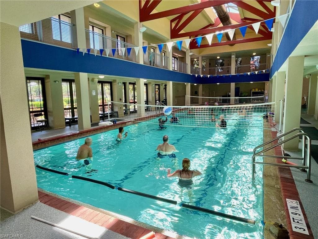 Indoor swimming pool featuring a volleyball net, overhead skylights, and multi-level architectural design with walking track balcony