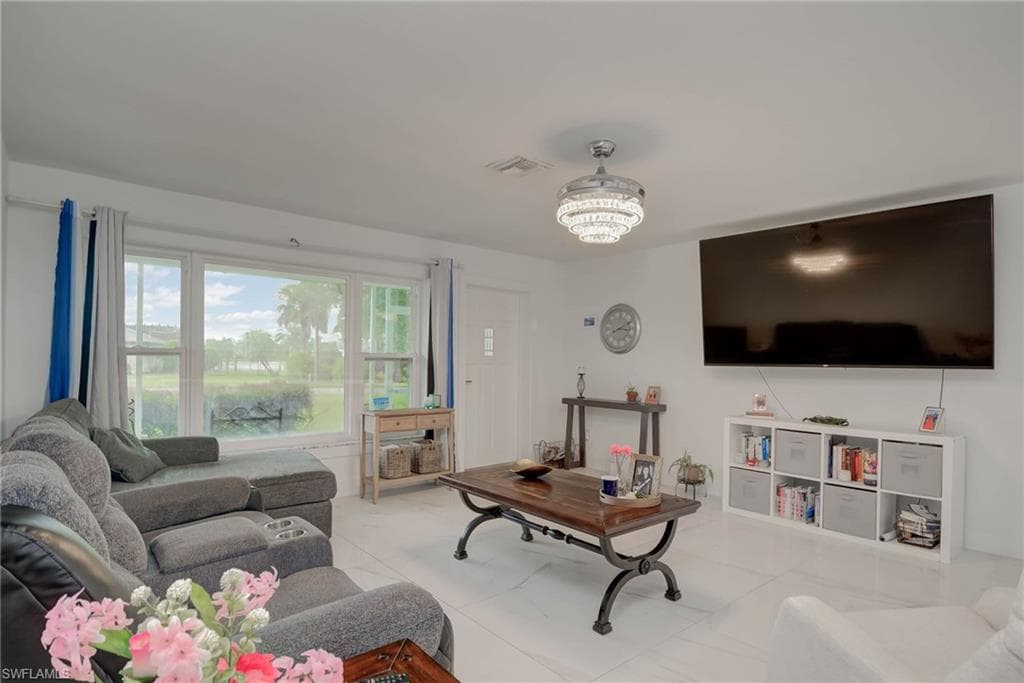 Spacious living area featuring large windows, white tile flooring, a contemporary ceiling light fixture, a wall-mounted television, and a built-in shelving unit