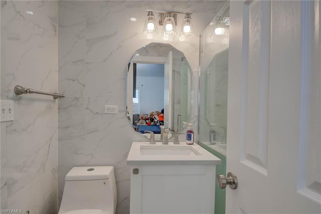 Bathroom featuring full-height marble-look tile, contemporary vanity with integrated sink, brushed nickel faucet, and a decorative frameless mirror