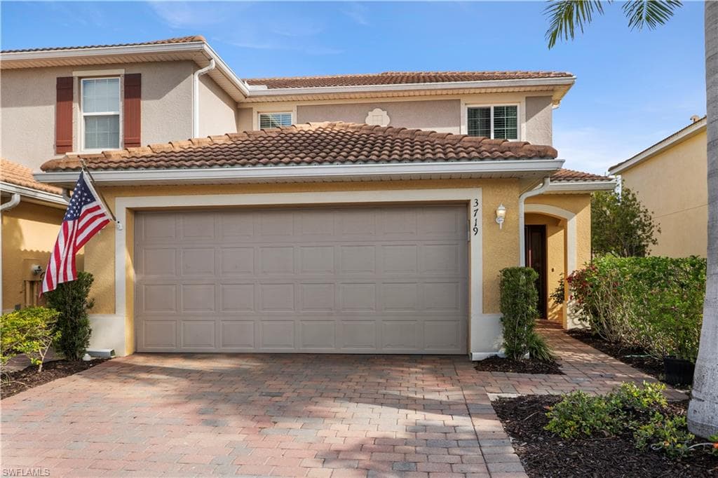 Mediterranean-style residence featuring a terracotta tile roof, paver driveway, and a two-car garage