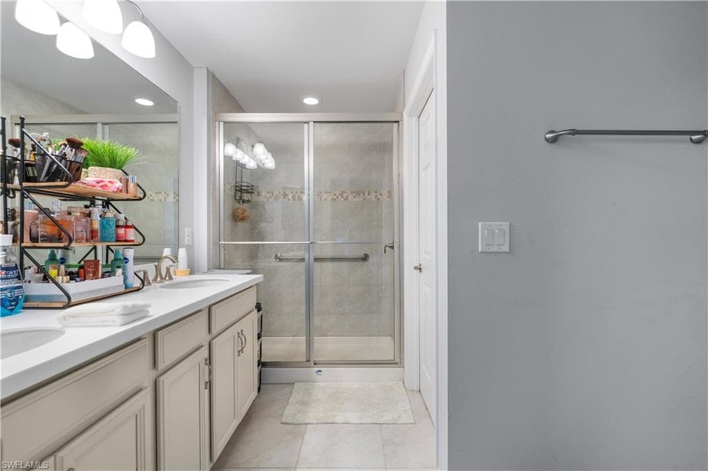 Bathroom featuring a glass-enclosed shower with decorative tile accent, dual vanity with undermount sinks, and tiled flooring