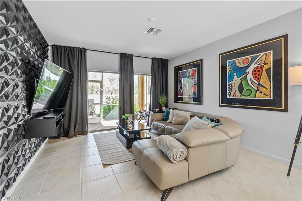 Living area featuring light-toned tile flooring, a textured accent wall with geometric patterns, and a wall-mounted media console