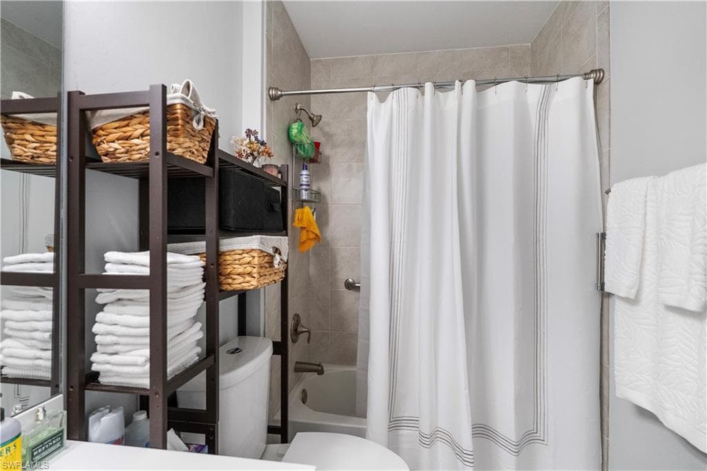 Bathroom featuring a shower-tub combination with tile surround, a white shower curtain with linear detailing, a wall-mounted towel bar, and a freestanding storage unit