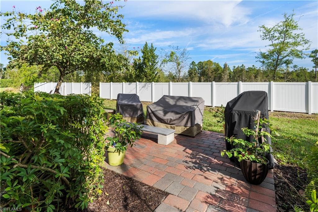 Brick paver patio with a low concrete bench, bordered by manicured shrubs