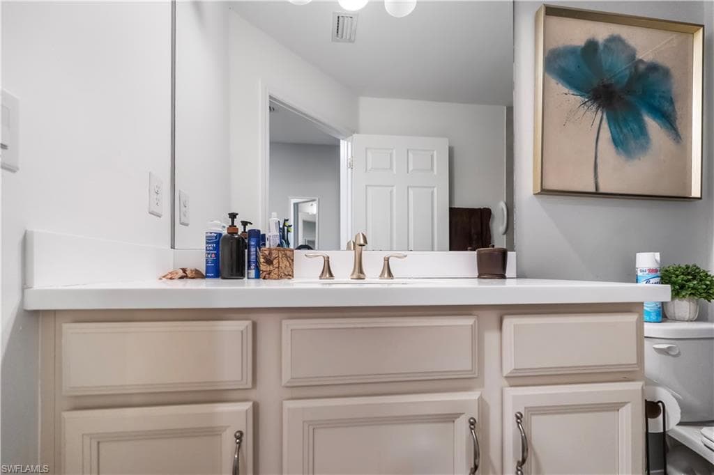 Vanity with a white countertop and integrated sink, bronze-finish faucet, and light-toned cabinetry with dark hardware