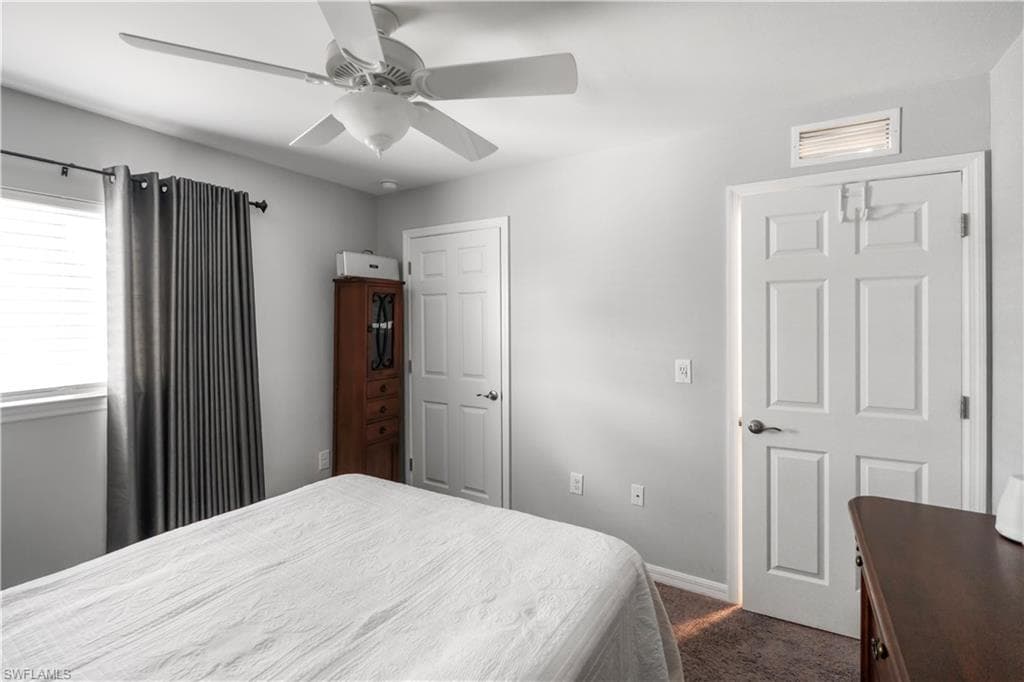 Interior space featuring a white ceiling fan with light fixture, light gray walls, and textured carpeting