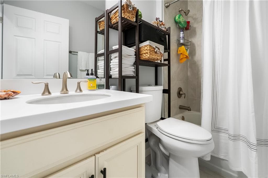 Bathroom featuring a vanity with a white countertop and undermount sink, brushed nickel faucet, light wood-finish cabinetry, a toilet, and a shower-tub combination with light-toned wall tile