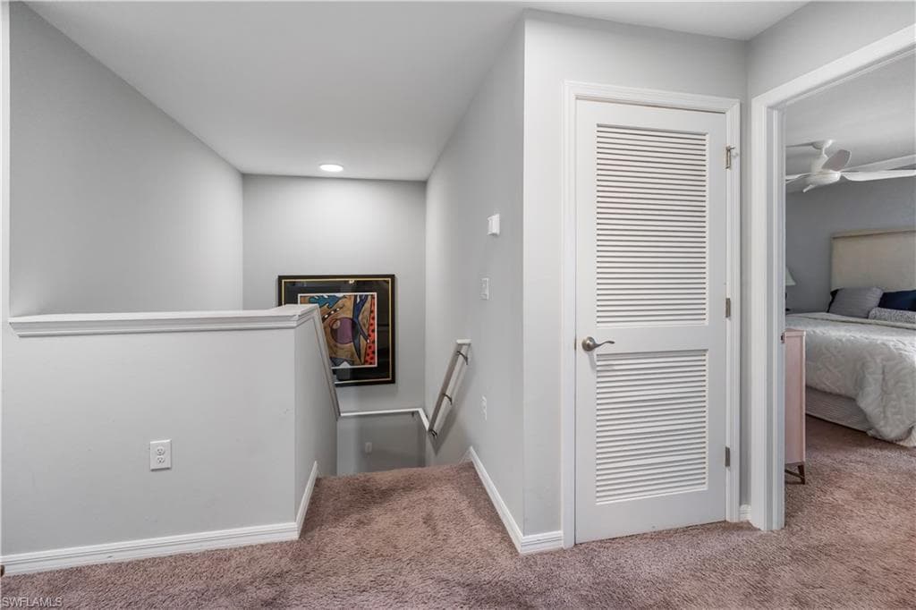 Carpeted landing featuring a white balustrade, recessed lighting, and a louvered interior door