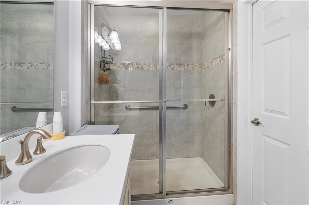 Bathroom featuring a glass-enclosed shower with tile surround, decorative mosaic accent band, and integrated grab bars